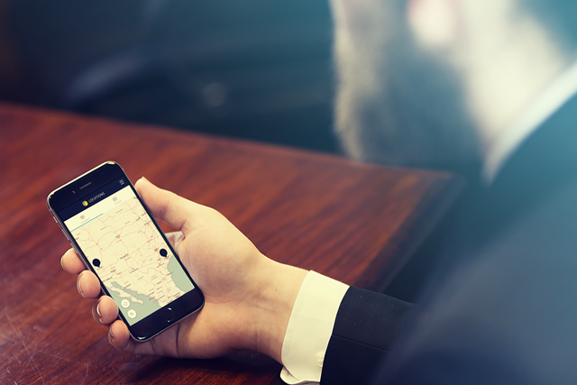 Hand holding smartphone which shows a map with a dropped pin indicating a location