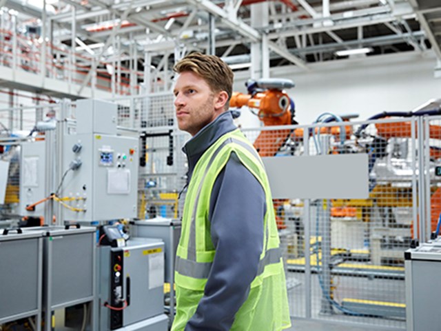 Worker in hi-vis standing in a car factory.