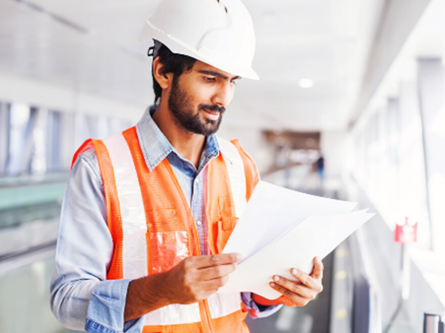 Worker in hi-vis and hard hat reviews documents
