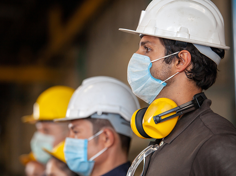 Workers wear protective face masks for safety in machine industrial factory.