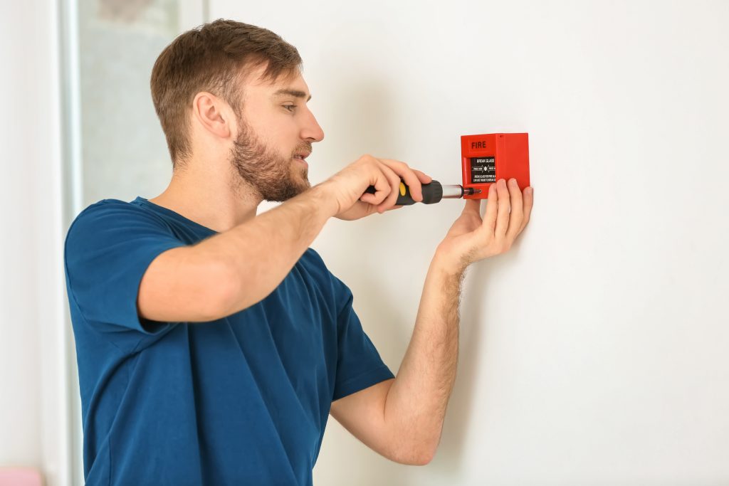 Young electrician installing fire alarm unit on wall