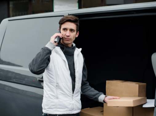 Professional courier near the car holding cartboard box calling the client by mobile phone near the office center